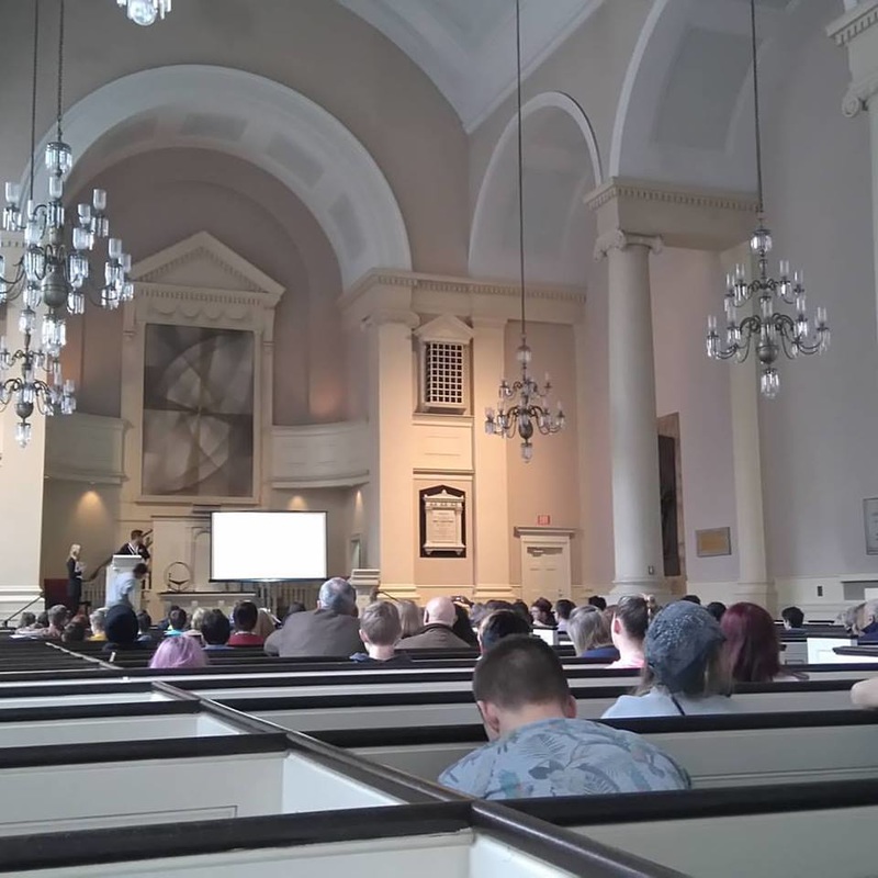 A photo of a very formal church service in a fancy church where all the pews, walls, and columns are white.