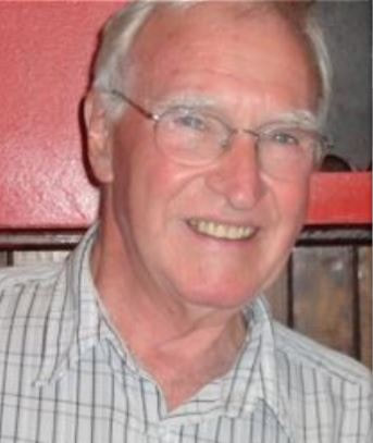 A headshot of Alex Campbell - an older white man with white hair, wearing a brown and white checked shirt.