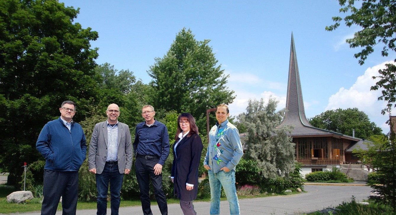Project partners standing on the proposed grounds for new affordable housing on the campus of First Unitarian Congregation of Ottawa.  From left to right: Rev Eric Meter (Minister, FirstU), Rodney Wilts (Theia Partners), Brent Nicolle (Board president, FirstU), Cathy Connor (Director of Housing Development, OAHS), Justin Marchand (CEO, OAHS). FirstU, with its iconic spire, appears behind the group, as they are standing in the parking lot that will, one day, be housing for over 200 families.