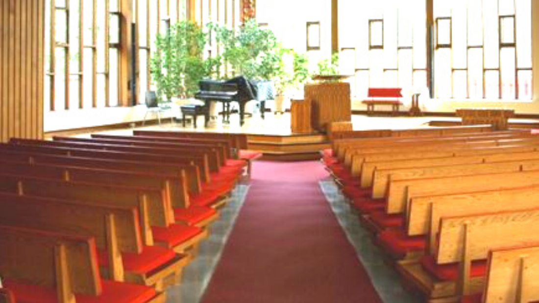 A photo of FirstU's sanctuary, as seen from the back of the room. The baby-grand piano is clearly visible at the front, in front of the windows.